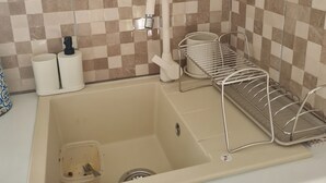 Et køkken med vask, opvaskestativ og hylde med krukker og blender.