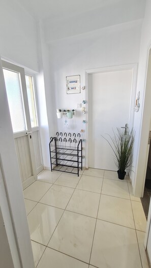 A hallway with a tiled floor, a metal coat rack, a door, and a potted plant.