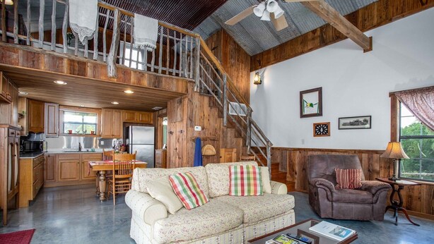 A spacious living area with a sofa, armchair, and coffee table, a kitchen with wooden cabinets, and a staircase leading to an upper level.