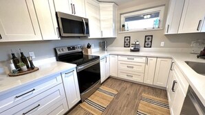 Una cocina moderna con armarios blancos, microondas, horno y un lavabo. Hay dos alfombras de madera en el suelo.