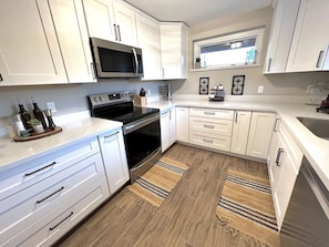 Una cocina moderna con armarios blancos, microondas, horno y un lavabo. Hay dos alfombras de madera en el suelo.