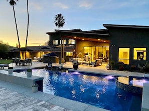 Una casa moderna con piscina, mobiliario exterior y un patio bien iluminado.