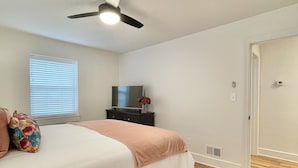 A bedroom with a bed, a ceiling fan, a TV, and a window with blinds. - Discover Tranquility at Carolina Cottage - Cozy 2-Bedroom Retreat in Hickory, NC (Hickory)