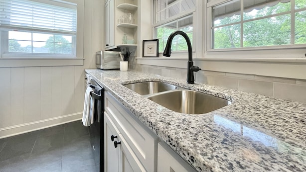 A kitchen with granite countertops, a stainless steel sink, white cabinetry, and a window with blinds. - Discover Tranquility at Carolina Cottage - Cozy 2-Bedroom Retreat in Hickory, NC (Hickory)