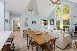 A spacious living area with a wooden dining table, a sofa, and a staircase leading to an upper level. - Cozy Sapphire Retreat | Fireplace • Dog Friendly (Sapphire)