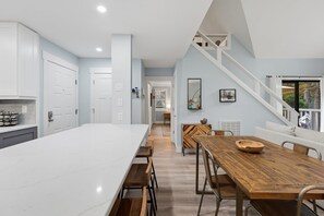 A modern kitchen with a large island, a dining area with a wooden table, and a staircase leading to an upper level. - Cozy Sapphire Retreat | Fireplace • Dog Friendly (Sapphire)