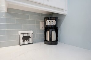 A kitchen with a Cuisinart coffee maker, a bear-shaped vent, and a white tiled backsplash. - Cozy Sapphire Retreat | Fireplace • Dog Friendly (Sapphire)