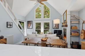 A dining area with a wooden table, chairs, and a fireplace. There is a staircase with a white railing leading to an upper level. - Cozy Sapphire Retreat | Fireplace • Dog Friendly (Sapphire)