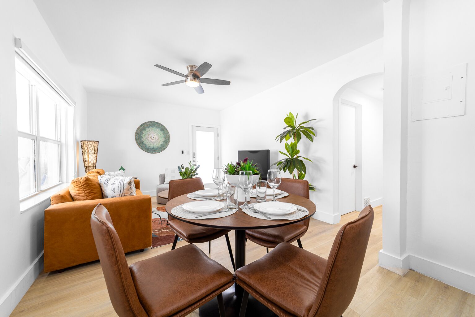 A modern dining area with a round table set for four, surrounded by brown leather chairs.