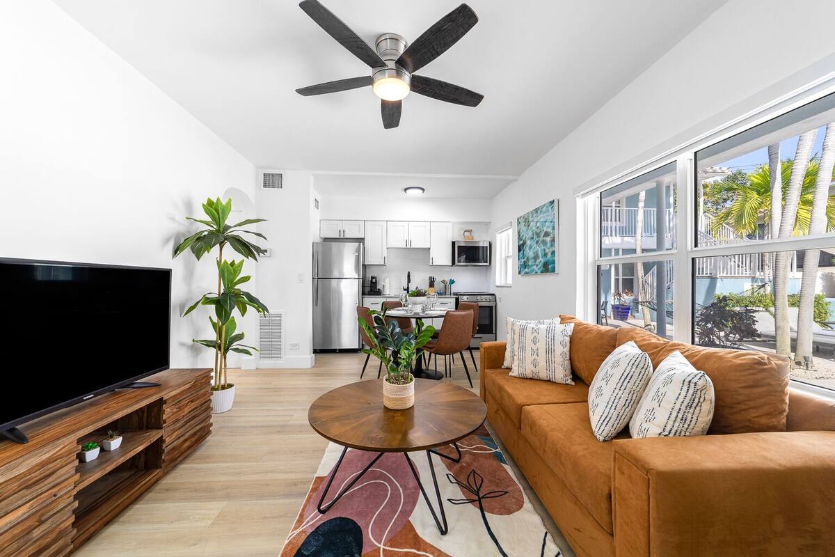 Un salon moderne avec un téléviseur à écran plat, un canapé marron, une table basse et un ventilateur de plafond.