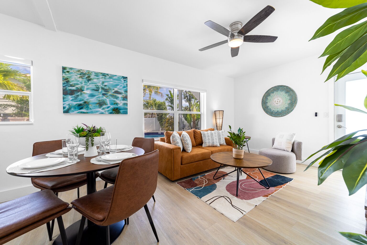 A modern living room with a dining area, a ceiling fan, and a view of the outdoors.
