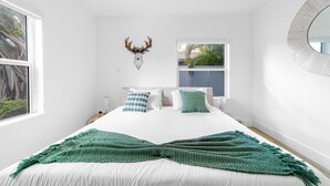 Un dormitorio con una cama grande, una ventana, un ciervo decorativo montado en la pared y un espejo redondo.