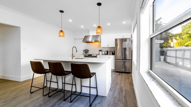 Una cocina moderna con una isla central, taburetes de bar, electrodomésticos de acero inoxidable e iluminación colgante.