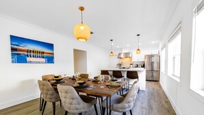 Una cocina moderna con electrodomésticos de acero inoxidable, una zona de comedor con una mesa de madera y sillas tapizadas, e iluminación colgante.