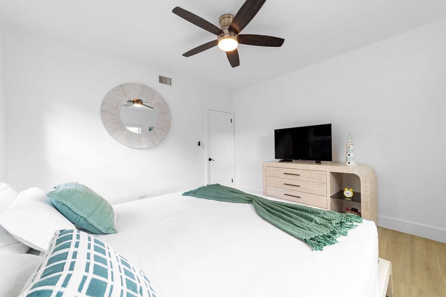 A modern bedroom with a bed, a ceiling fan, a TV on a wooden cabinet, and a wall-mounted mirror.