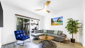 Una sala de estar moderna con un sillón azul, un sofá gris, una mesa de centro redonda y un ventilador de techo.