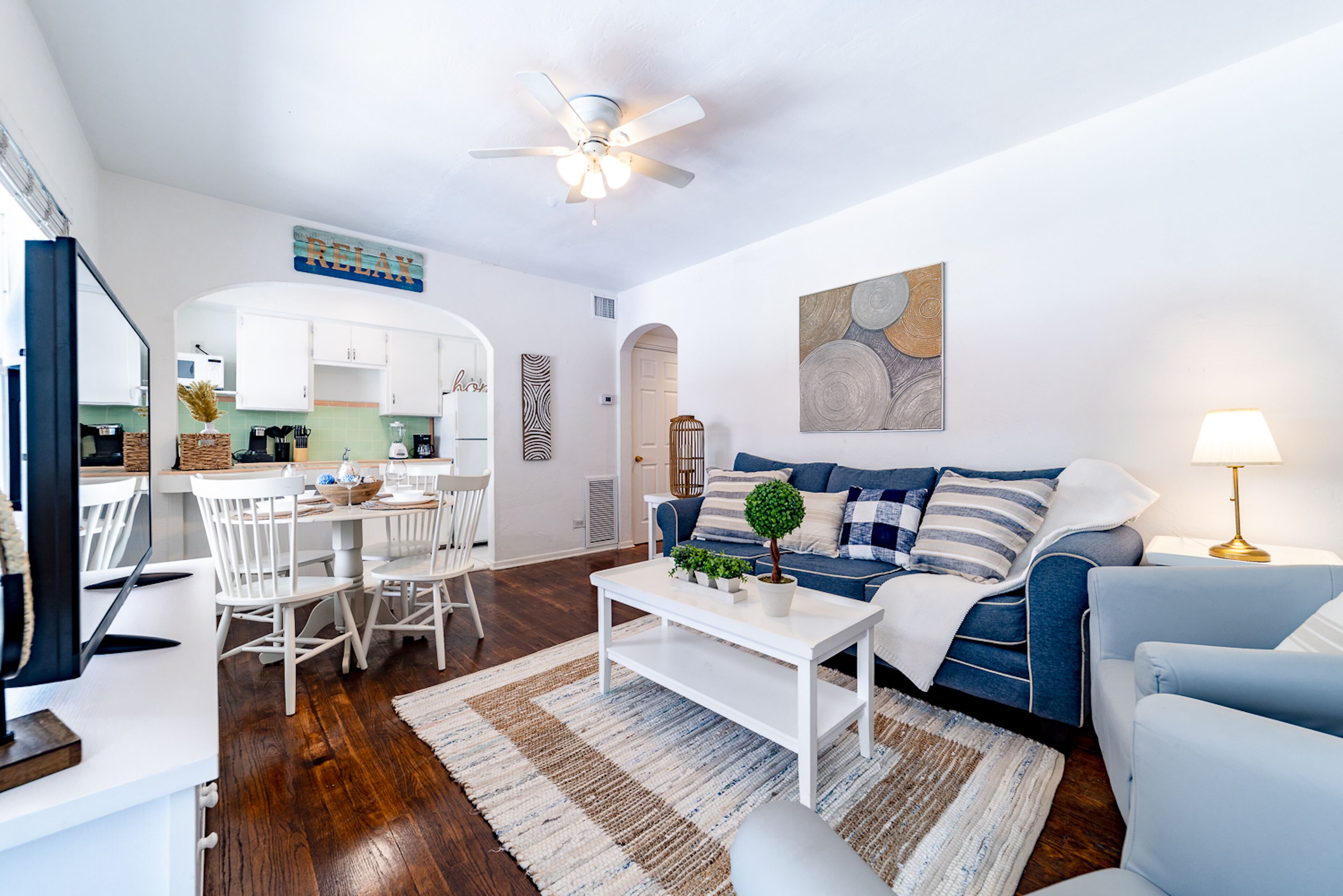 A modern living room with a white coffee table, blue sofa, and a dining area with white chairs.