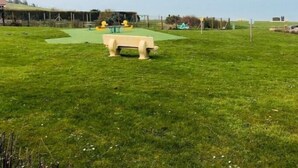 A grassy outdoor area with a bench, playground equipment, and a building in the background. - Maison Individuelle en Bord de mer (Saint-Martin-en-Campagne)