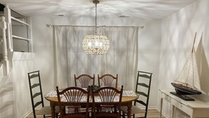 Un comedor con una mesa redonda, seis sillas, una araña de techo, un modelo de velero y una escalera.