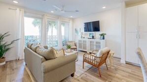 Un salon spacieux comprenant un canapé, un fauteuil en osier, une table basse et un téléviseur fixé au mur.