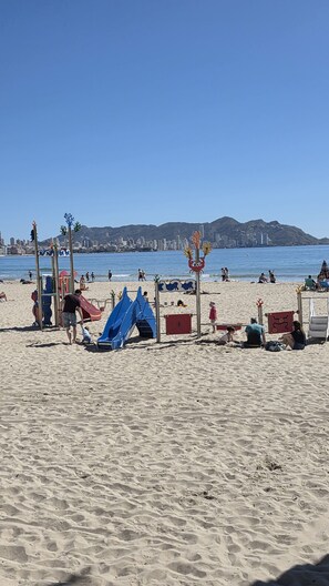 A beach with a playground, including slides and climbing structures, and a city skyline in the background.