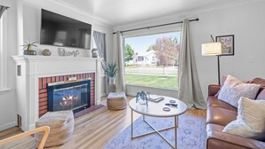 A living room with a fireplace, a sofa, a coffee table, and a large window with a view of the outside. - Remodeled home with vintage charm. Centrally located near downtown Idaho Falls. (Idaho Falls)