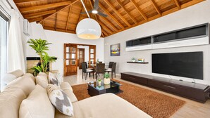 A modern living room with a high ceiling, a flat-screen TV, a sofa, a coffee table, and a dining area. - Villa in the mountain with views and pool (Adeje)