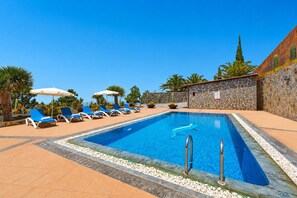 Une piscine rectangulaire avec un mur en pierre et un palmier en arrière-plan.