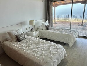 A hotel room with two beds, a nightstand, a lamp, and a view of the sea.