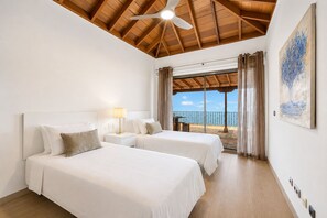 Une chambre d’hôtel avec deux lits, un ventilateur de plafond, un balcon avec des rideaux et un tableau au mur.
