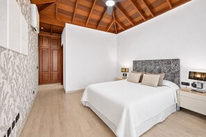 Un dormitorio con techo de madera, cama con cabecera estampada de cebra, lámparas de noche y un armario.