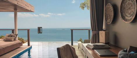 A room with a view of the sea, a wooden desk, a laptop, and a bed with a view.