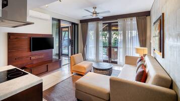 Una habitación de hotel moderna con televisor de pantalla plana, un panel de madera decorativo, ventilador de techo, sofá, mesa de centro y vistas al exterior.
