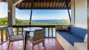 A balcony with wicker chairs, a table, and a sofa with a view of the ocean and hills. - Sundancer Residences & Villas Lombok (Sekotong Barat)