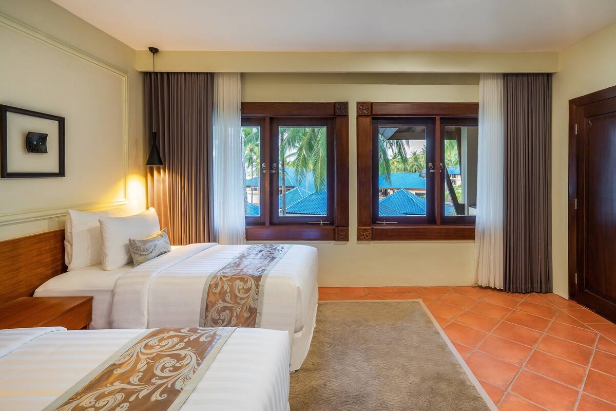 A hotel room with two beds, a desk, and a view of a pool and palm trees.