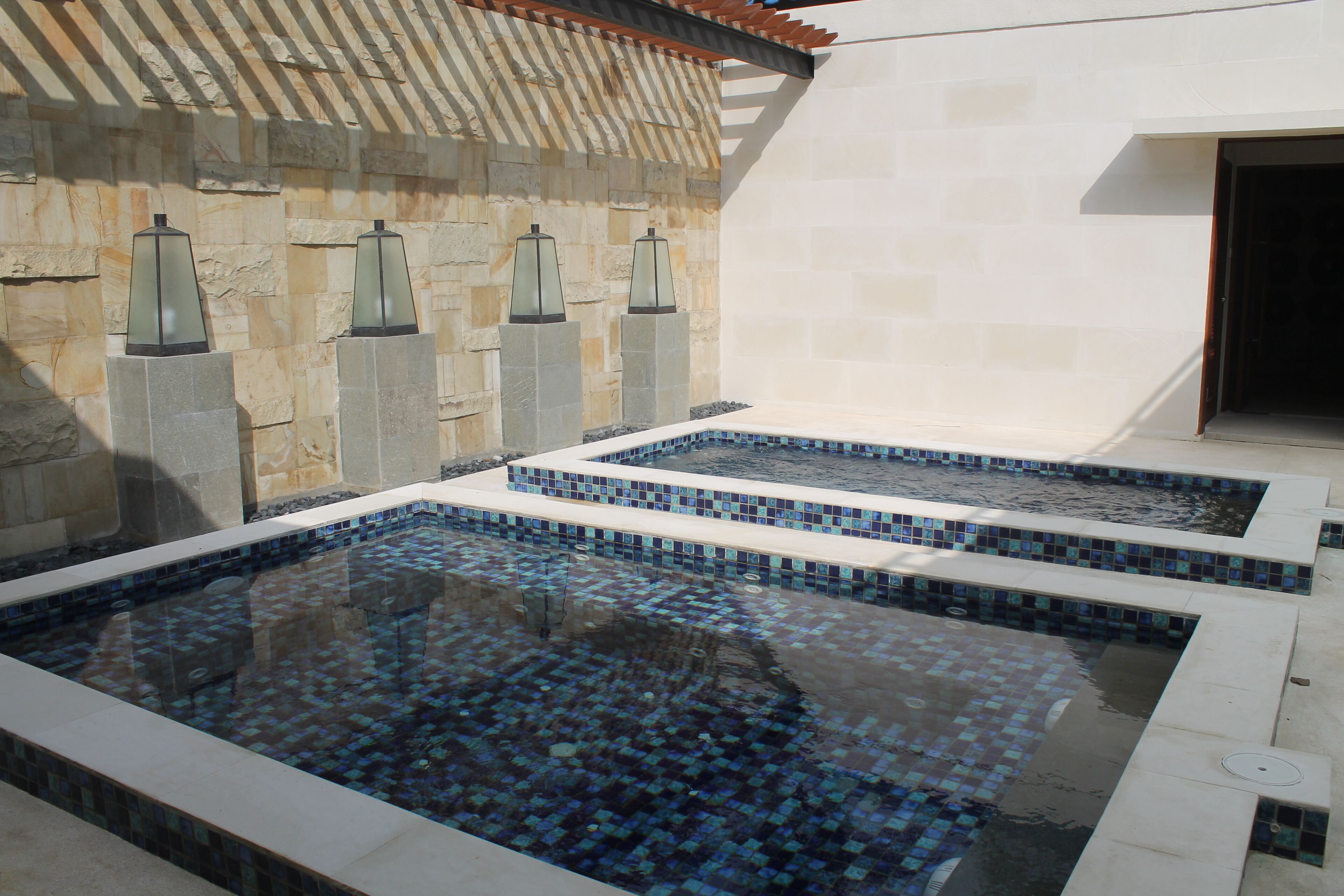 Ein Wellnessbereich mit zwei rechteckigen Pools, Steinwänden und dekorativen Laternen.
