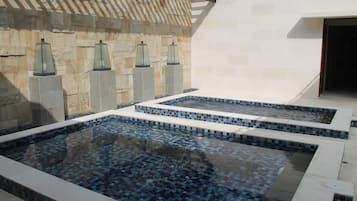 Ein Wellnessbereich mit zwei rechteckigen Pools, Steinwänden und dekorativen Laternen.