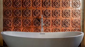 A modern bathroom with a freestanding bathtub, a tiled wall with intricate patterns, and a stone floor.