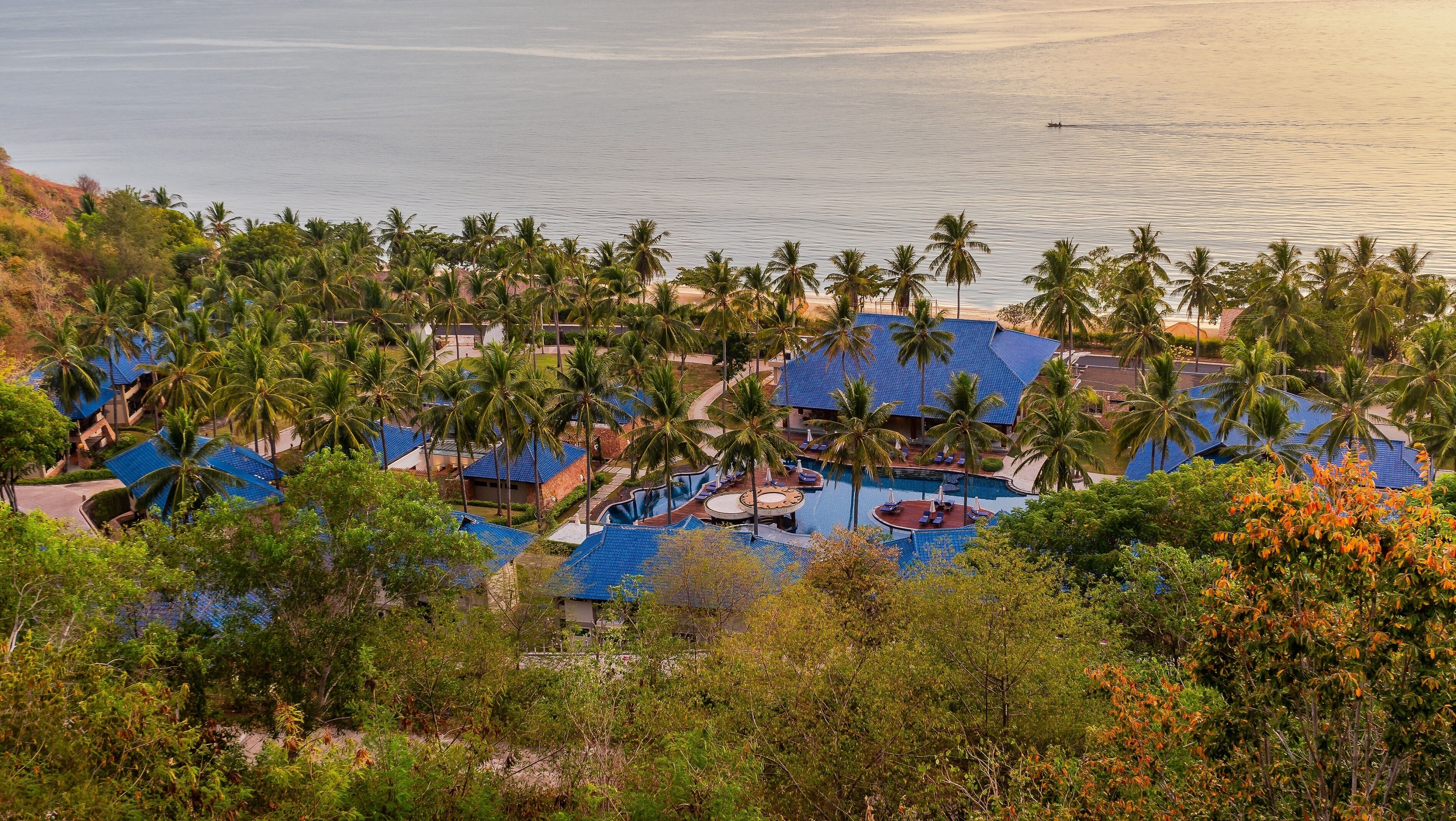 A resort with multiple blue-roofed buildings, a central swimming pool, and palm trees.