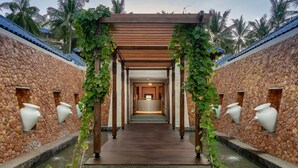 A pathway leading to a spa area with a wooden pergola, stone walls, and water features. - Sundancer Residences & Villas Lombok (Sekotong Barat)