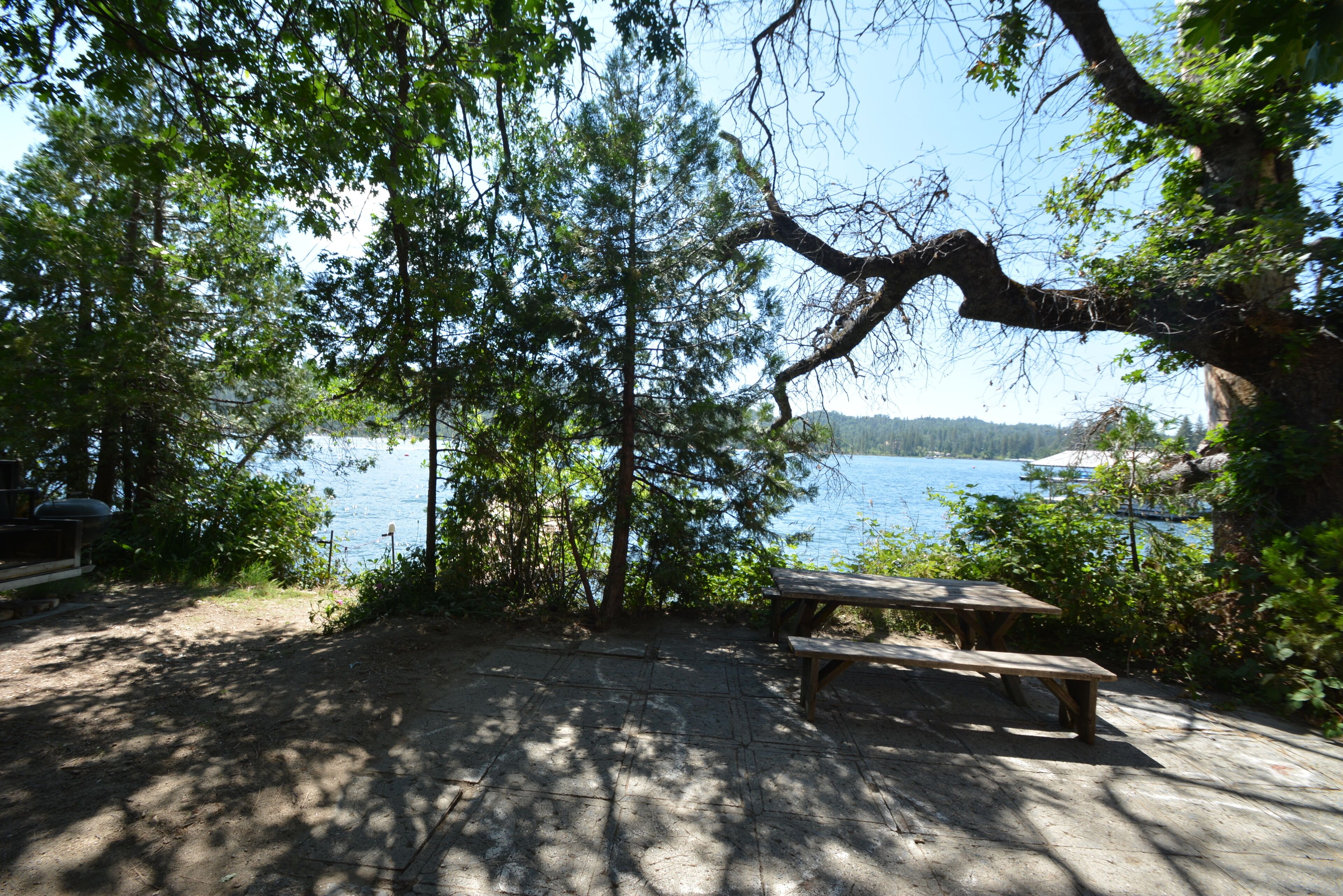 Une table de pique-nique et un banc au bord d’un lac, entourés d’arbres, sous un ciel dégagé.