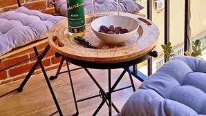 Ein Balkon mit rundem Tisch, zwei gepolsterten Stühlen, einer Weinflasche und einer Oliven-Schale.
