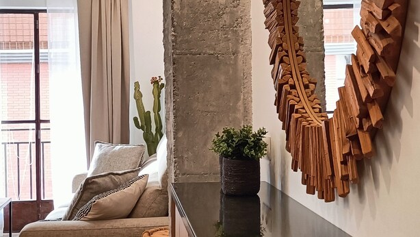 Ein modernes Wohnzimmer mit großem Spiegel, einer Couch, einer Kakteenpflanze und einer strukturierten Wand.