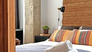Ein Schlafzimmer mit einem großen Bett, einem Kopfteil mit Stammeskunst, einem Nachttisch mit Lampe und Blick ins Freie.