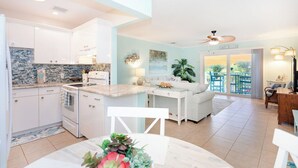 A modern kitchen with white cabinets, a granite countertop, and a dining area with a white table and chairs. - Private Beach Retreat! Luxurious Bedding, Relaxing Pool, Best Sunsets, Fast WiFi (Key Colony Beach)