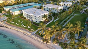 An aerial view of a resort with multiple buildings, a beach, and palm trees. - Private Beach Retreat! Luxurious Bedding, Relaxing Pool, Best Sunsets, Fast WiFi (Key Colony Beach)