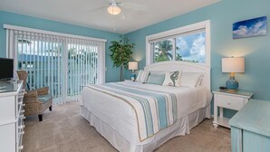 A bedroom with a large bed, a ceiling fan, a window with blinds, a nightstand with a lamp, and a dresser. - Private Beach Retreat! Luxurious Bedding, Relaxing Pool, Best Sunsets, Fast WiFi (Key Colony Beach)