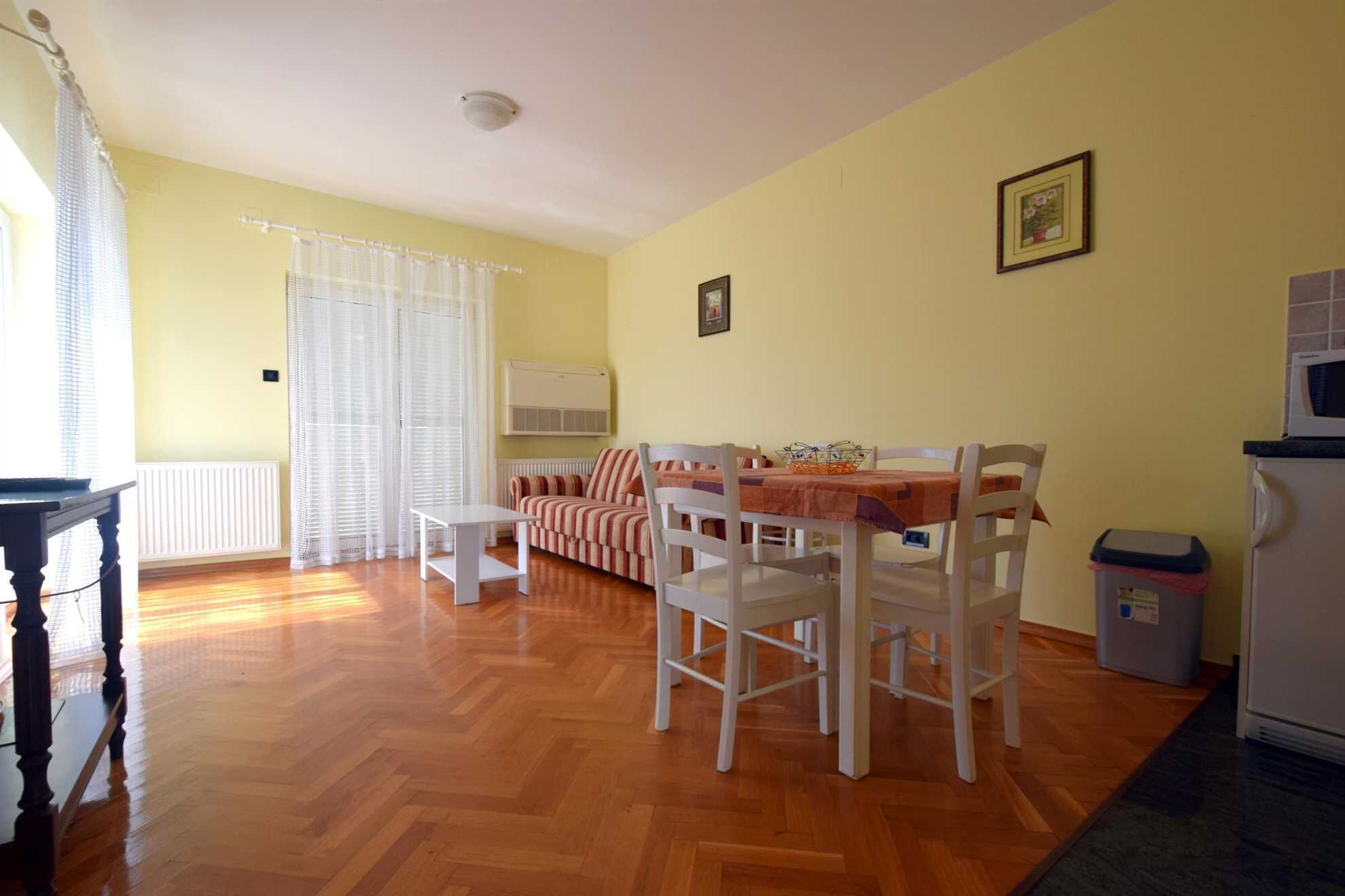 Un salon comprenant un canapé, une table à manger, des chaises, un radiateur, une fenêtre avec des rideaux et un réfrigérateur.