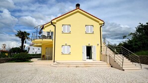 Un bâtiment jaune à deux étages, doté d’un balcon, d’un escalier et d’une cour dallée.