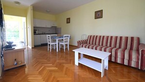 A living room with a sofa, a dining table with chairs, a kitchen area, and a wooden floor. - Apartment Luka 2 with Balcony (Malinska)